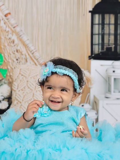 A smiling baby girl in a blue tulle dress, enjoying the whimsical boho-themed studio setup. The combination of textures and props makes for a visually interesting and beautiful photo.