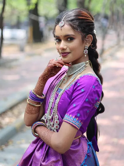 A portrait of a young woman with intricate henna on her hands, dressed in a traditional South Indian langa voni.