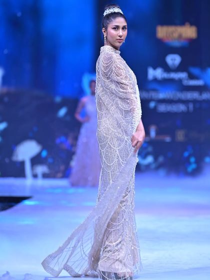 This gown is a symphony of craftsmanship, featuring a fully beaded tube silhouette with an attached floor-length sheer cape. The intricate pearl and katdana work creates a mesmerizing, liquid-like shimmer.