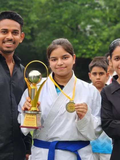 This student, a blue belt, shows her trophy and medal with pride. Her achievement at the district championship is an inspiration to all.