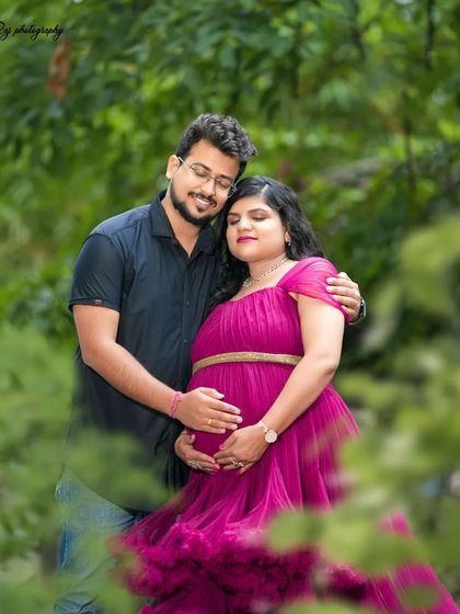 A tender moment between a couple in a garden setting. The mother-to-be is wearing a wine-colored ruffled gown.