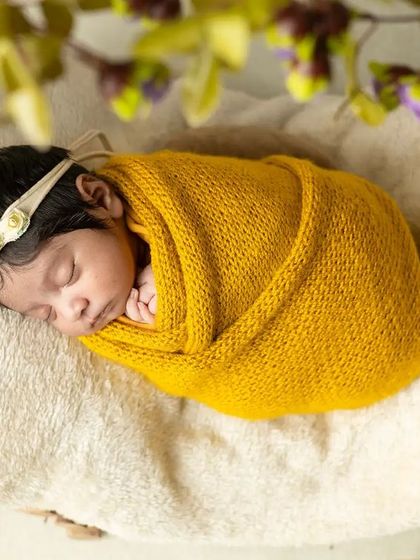 A newborn rests peacefully in a rustic, circular wooden prop adorned with leaves and flowers, showcasing a natural and earthy style of newborn photography.