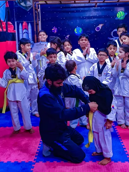 A proud moment for any student is earning their next belt. Here, I am helping a young student tie her new yellow belt during our belt distribution ceremony, marking a new chapter in her training.