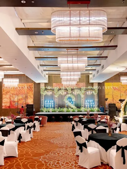 A full view of a large ballroom set up for a corporate event. The image shows the main stage in the distance, with round tables arranged for guests, demonstrating our capability in managing large-scale event layouts and decor.