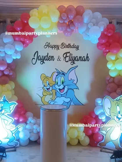 A classic Tom and Jerry theme for a joint birthday party. The setup includes a colorful balloon arch and light-up cutouts of the iconic cat and mouse duo.