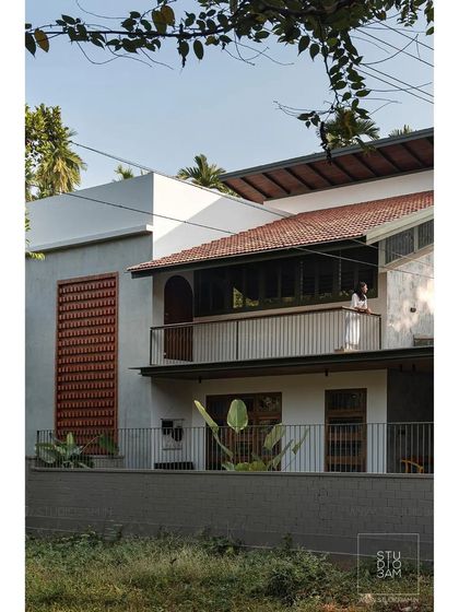 The facade of the 'Olive Dwelling' is a complex play of textures and materials, including exposed brick jali, smooth plaster, and a traditional tiled roof.
