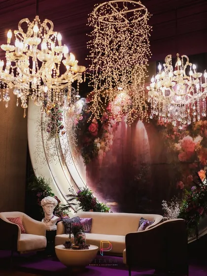 A lounge setup that is the definition of romantic opulence. A curved backdrop with a floral mural, classic bust sculpture, and cascading crystal lights create a dreamy, artful space for guests to relax.