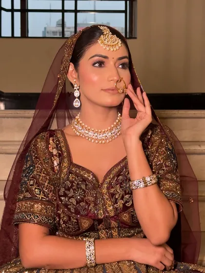 A profile shot showcasing the complete bridal look, including the delicate nath and maang tikka. The makeup is designed to look flawless from every angle.