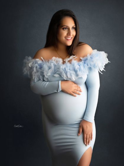 A beautiful, happy portrait of a mom-to-be in a light blue, form-fitting gown with a feathered neckline.