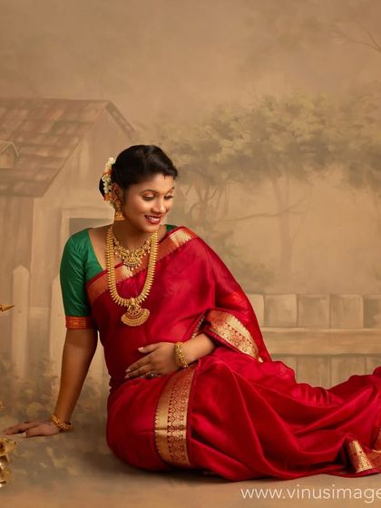 Seated next to a traditional brass lamp, or 'diya', this mother-to-be in her red saree looks serene and content. The painted backdrop adds a rustic, nostalgic village feel.