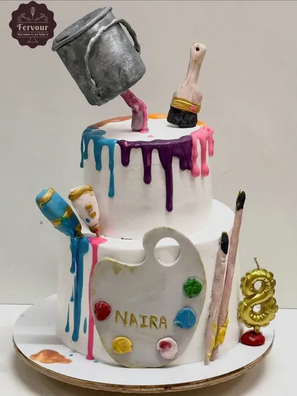 This two-tier anti-gravity cake was designed for a young artist. It features an edible paint bucket that appears to be pouring colourful drips down the sides, surrounded by fondant paintbrushes, tubes, and a palette personalized with her name.