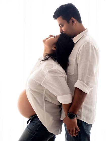 A tender forehead kiss is such a classic and heartfelt pose for a couple's maternity photoshoot. This was captured using a simple white shirt and jeans styling.