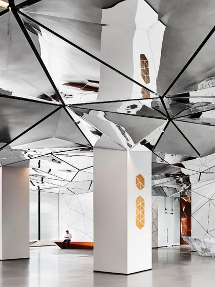 The lobby's design uses a limited palette of white, grey, and metallic tones, punctuated by warm accents. This allows the geometric forms and reflective surfaces to be the main focus.