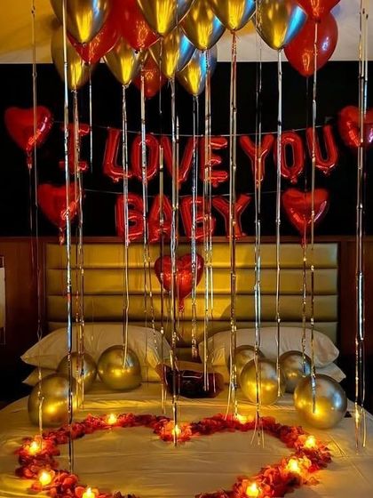 A close-up of the bed decor, featuring "I Love You Baby" foil balloons, a heart of rose petals, and metallic balloons for a touch of glamour.