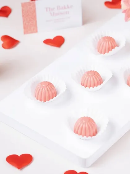 Pink bonbons arranged on a clean white surface with heart confetti. This minimalist and romantic styling is perfect for Valentine's Day confectionery.