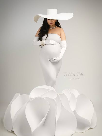 A frontal view capturing the full bloom effect of the gown. The mother cradles her bump, a picture of grace and anticipation, enveloped in petals.