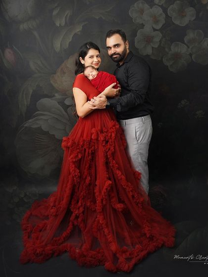A beautiful family portrait with their newborn son. The mother's stunning red gown pops against the dark floral backdrop, creating a dramatic and romantic image.