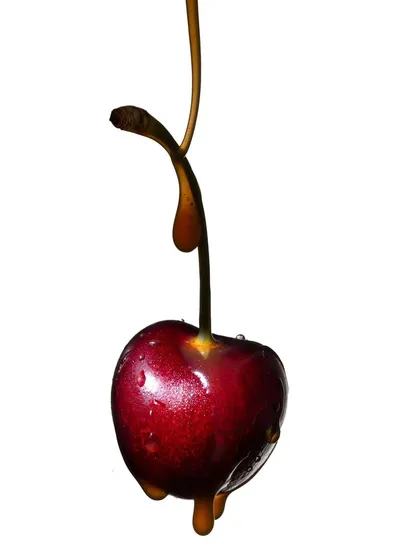 A macro shot of a single cherry with a delicate stream of caramel dripping down. The focus is on the beautiful curve of the caramel and the deep red of the cherry, creating a simple and elegant composition.