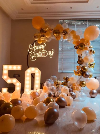 Celebrating half a century in style! This gorgeous 50th birthday setup features a soft peach and gold balloon arch, a neon sign, and large marquee numbers.