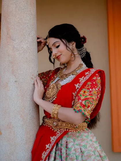 A smiling portrait of actress Niveditha Gowda in a stunning red half saree. The shot captures her joyful expression and the intricate details of her bridal look.