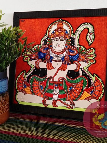 The framed 14x14 inch Anjeneyar painting, placed in a home setting. The powerful presence of Hanuman in this meditative form brings a sense of peace and strength to the environment.