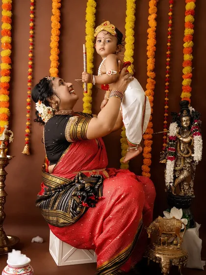 A joyful mother lifts her baby high, both smiling, capturing a moment of pure happiness during their Janmashtami session.