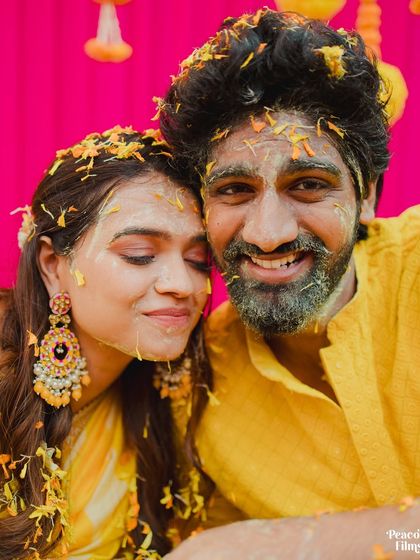 A sweet and candid portrait of the couple, their faces close together, covered in flower petals and turmeric.