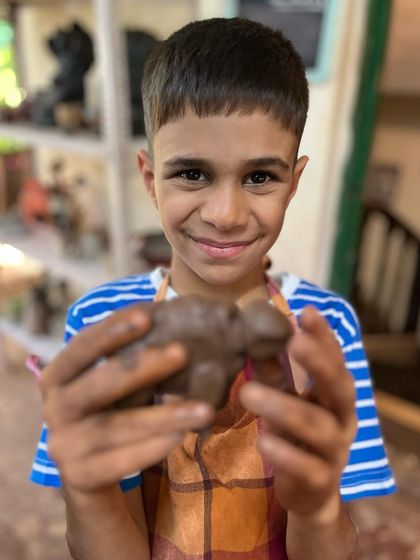 A happy smile from a young potter holding his finished clay turtle. Our workshops for kids focus on fun, imagination, and the joy of making something with their own hands.