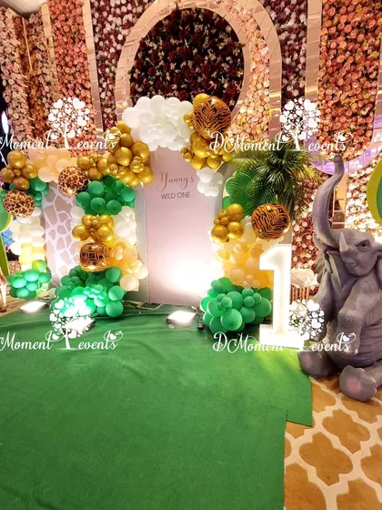 A photo corner at the jungle safari party, featuring a green grass floor, an elephant prop, and a backdrop with gold and green balloons.