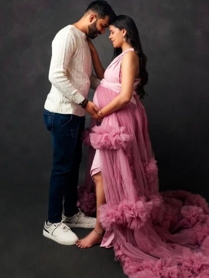 An intimate and tender moment between a couple, with the mom-to-be in a beautiful dusty rose ruffled gown.