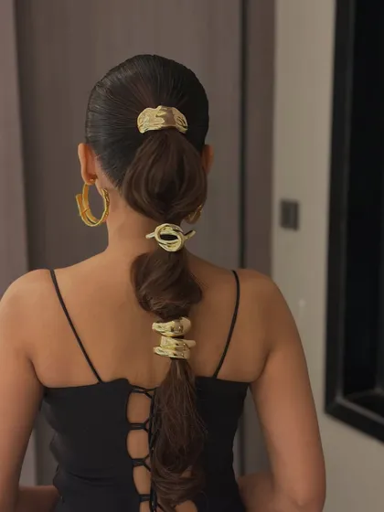 A close-up of the modern bubble ponytail with abstract gold accessories. This shows how contemporary jewelry can create a unique and edgy hairstyle.