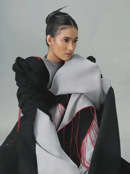 The architectural outfit is paired with a sharp, minimalist white liner and spiky hair for a cohesive, avant-garde look.
