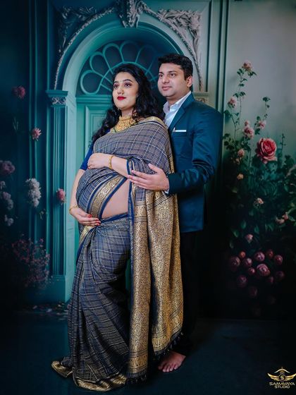 A standing portrait of the couple, with the partner's arms wrapped lovingly around the mother-to-be. Their traditional attire looks stunning against the moody, romantic backdrop.