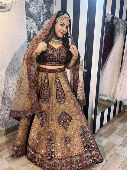 A client trying on a beautiful maroon and gold bridal lehenga in our store. This image shows the complete look with the dupatta draped, giving a real sense of how it feels to wear.