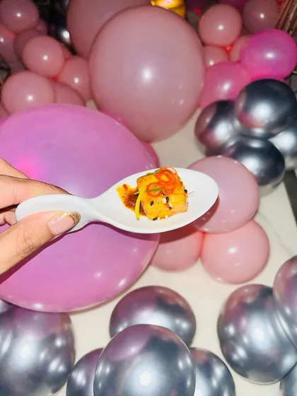 A single, flavourful bite of a salmon appetizer, held up against the party's pink and silver balloon decor.