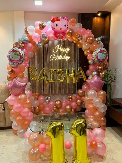A Hello Kitty theme for an 11th birthday, featuring a circular balloon arch in pink and rose gold with the birthday girl's name in foil letters.