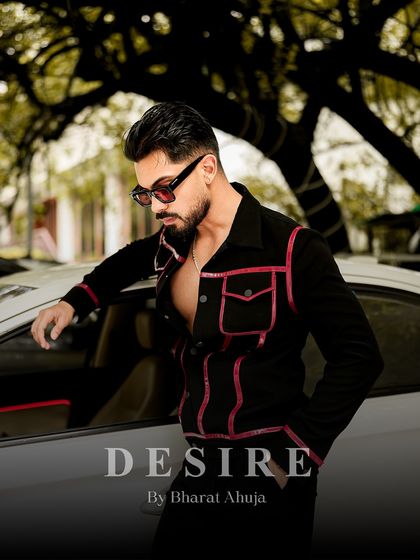 Confidence tailored to perfection. This shot shows the black and red piped jacket in a relaxed pose, leaning against a car.