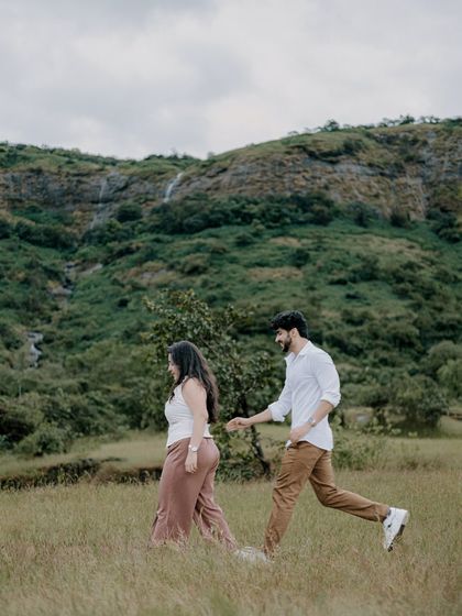 A candid moment of the couple walking through a field, with the groom playfully leading the way. This shot captures their natural interaction and the beauty of the surrounding landscape.