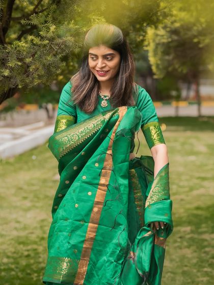 A full-length shot capturing the graceful flow and rich color of a green silk saree in a beautiful park setting.