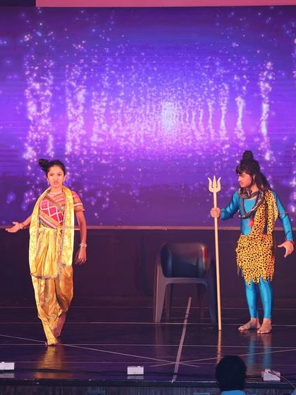 A theatrical moment from our Shiv prayer dance, showing an interaction between two characters on stage, set against a celestial background.
