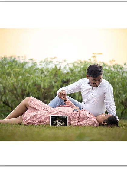 A relaxed, romantic pose on the grass, with the sonogram picture resting on the baby bump.