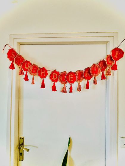 This custom "Shubh Deepawali" bunting is made from crochet and can be used year after year. This one, in festive red and gold, is hanging on a door, ready to welcome guests during the festival.