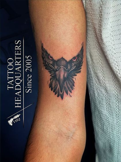 A stylized eagle head tattoo with piercing red eyes, symbolizing vision and power.