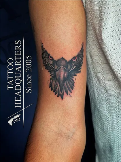 A stylized eagle head tattoo with piercing red eyes, symbolizing vision and power.