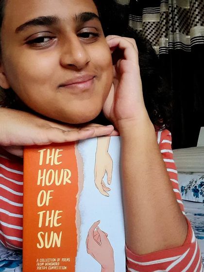 A poet poses with 'The Hour of the Sun,' the anthology containing her poem 'Rise and Fall.' Her journey from dream to reality is a story we are proud to be a part of.
