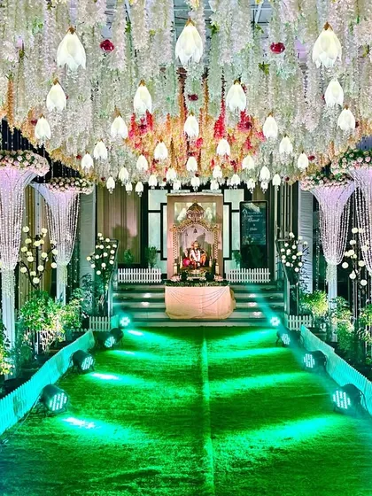 A simple and classy reception entrance. The walkway is lined with pearl-like cascades and floral pillars, leading guests toward a canopy of hanging white flowers.
