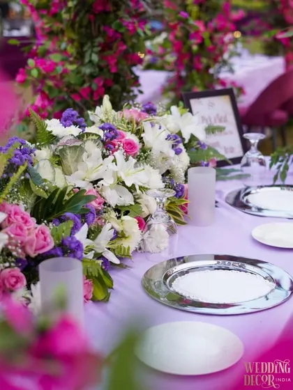 A close-up of a table setting at the purple velvet engagement. A beautiful floral centerpiece sits on a lavender tablecloth, with silver charger plates adding a touch of metallic shine.