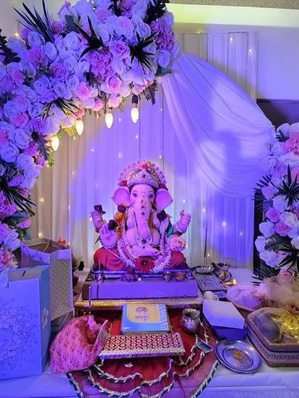 A beautiful floral arch in shades of lavender and white, with a soft white drape as a backdrop. The purple lighting enhances the color scheme and creates a serene, evening-ready look.