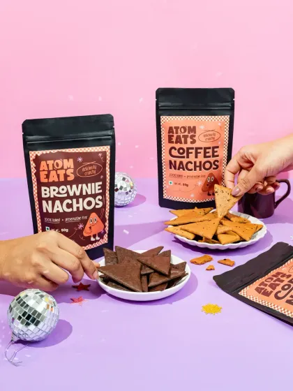 A fun, party-themed shot of Atom Eats Brownie and Coffee Nachos. The hands reaching in to snack and the disco balls create a celebratory vibe perfect for social media.