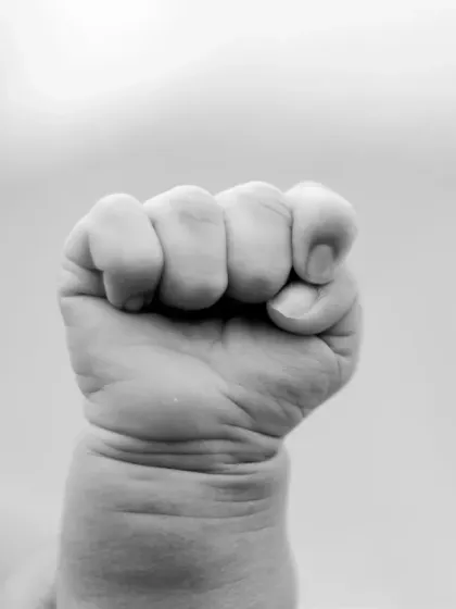 A tiny, perfect fist. This black and white macro shot highlights the wrinkles and details of a newborn's hand.